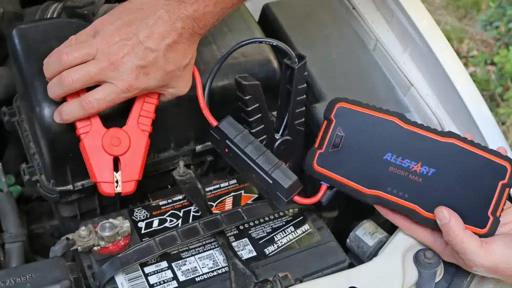 A view of a person holding the car's jumper cable with a battery inside the engine