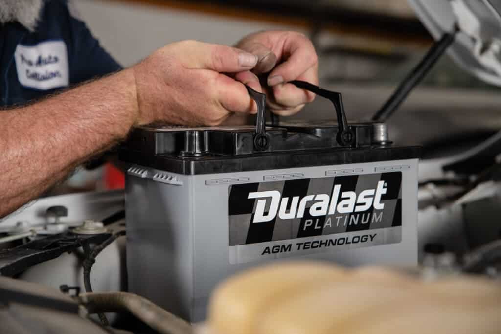 hands of a mechanic holding a duralast battery in gray color