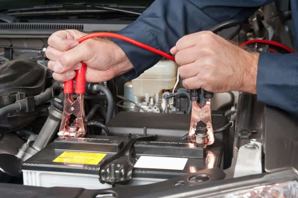 male hands holding jumpers and working with car battery 