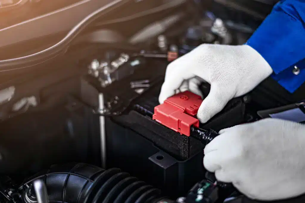 close up of male hands wearing gloves checking the car battery terminals