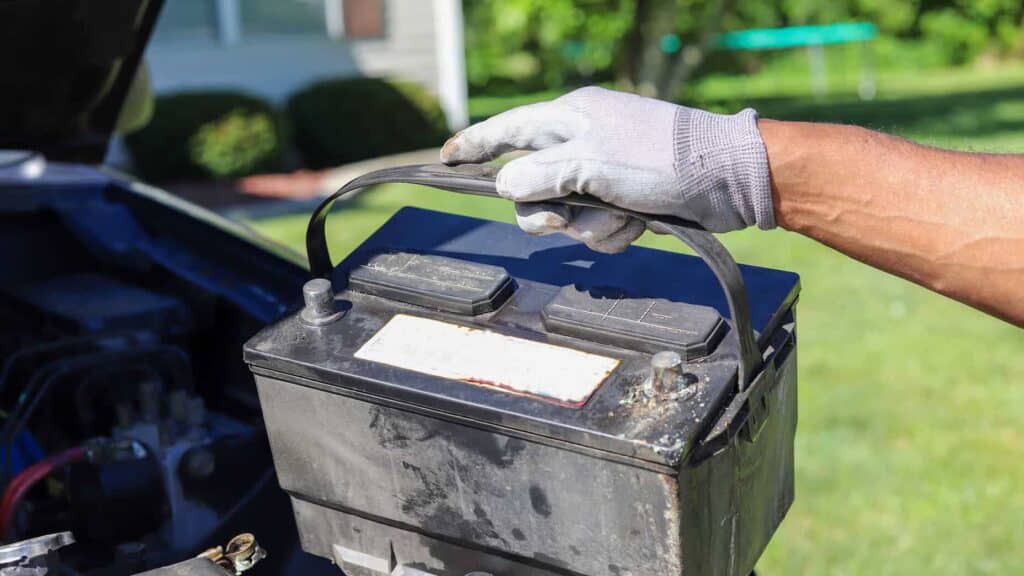 male hand wearing glove and holding a car battery