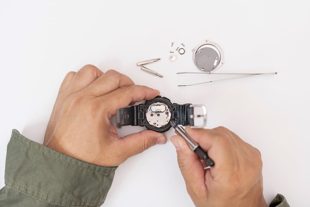 A Man Use Pliers To Clamp The Digital Watch Battery